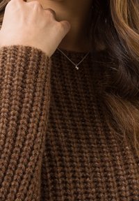 Pull en maille brun avec une texture côtelée. Un collier en argent avec un petit pendentif est visible près de l'encolure.