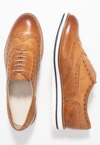 Richelieus en cuir tan avec des perforations, semelle blanche contrastante avec une bande navy, design à lacets, bouts ronds et finition texturée.