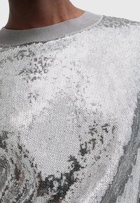 Top in paillettes argento con colletto girocollo a coste grigio, caratterizzato da una superficie scintillante e riflettente con un motivo circolare su tutta la superficie.