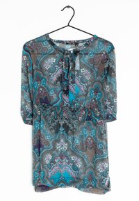Blouse transparente à motifs avec un design paisley bleu, gris et violet. Dotée d'un col rond, de détails à nouer et de manches trois quarts.