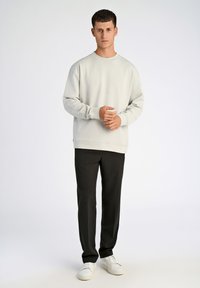 Sudadera gris claro con cuello redondo, puños acanalados y un corte relajado. Combinada con pantalones negros y zapatillas blancas.