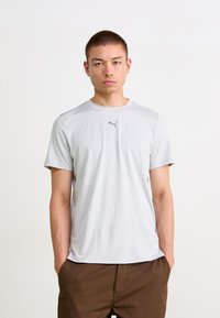 Světle šedé tričko s krátkým rukávem z hladkého, lehkého materiálu. Na hrudi je malé černé logo Puma. Klasický kulatý výstřih, nezdobený design.