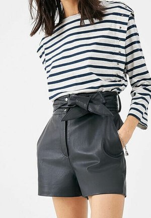 Femme portant un short en cuir noir taille haute avec ceinture nouée et une chemise blanche à manches longues avec des rayures horizontales bleu marine.