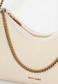 Borsa a spalla in pelle crema con design curvo, dotata di tracolla in catena dorata e chiusura con zip. Logo del marchio impresso sulla parte anteriore.