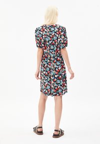 Robe florale avec des manches bouffantes courtes, taille cintrée, fond noir et motifs de fleurs multicolores ; modèle portant des sandales plates.