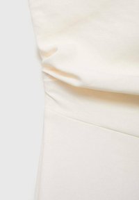 Krämfärgad tyg med en slät textur, med mjuka draperingar vid midjan och en ren, skräddarsydd form. Inga synliga detaljer eller mönster.