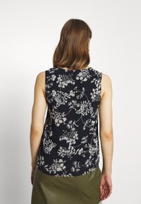 Bloemige mouwloze blouse in marineblauw met crèmekleurige botanische patronen, ronde halslijn en een losse pasvorm, die eindigt op de heupen. Zachte stoftextuur.