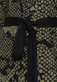 Tessuto di maglia nera con un design di stampa leopardata dorata, caratterizzato da una cintura nera annodata in vita. Accenti dorati texturizzati esaltano il motivo.