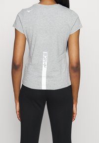 Camiseta deportiva gris de manga corta, con escote redondo, que presenta una franja vertical blanca y un detalle del logo en la espalda. Material texturizado.