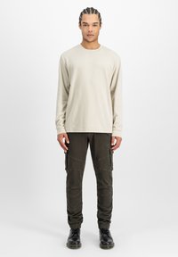 Un tricou lung bej deschis cu guler rotund, asortat cu pantaloni cargo negri cu buzunare și manșete elastice, purtat cu cizme negre.