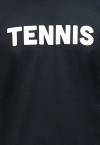 Μαύρο βαμβακερό μπλουζάκι με μεγάλο, έντονο λευκό κείμενο που γράφει «TENNIS» στη μπροστινή πλευρά. Ομαλή υφή, casual εφαρμογή.