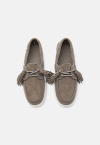 Par de mocasines de ante color topo con suelas blancas, cordones con borlas y detalles cosidos, vistos desde arriba sobre un fondo liso.