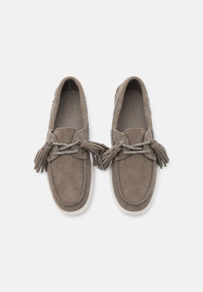Ζευγάρι μοκασίνια σουέτ σε ταουπε απόχρωση με λευκές σόλες, κορδόνια με φουντίτσες και ραμμένες λεπτομέρειες, εμφανιζόμενα από πάνω σε απλό φόντο.