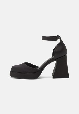 Chaussure à talon haut plateforme noire avec bout fermé, talon épais en bloc et bride de cheville avec fermeture à boucle, vue de côté.