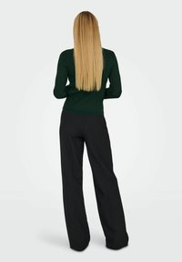 Mörkgrön ribbad långärmad topp i kombination med svarta vida byxor. Outfiten har en figurnära design och en slät textur.