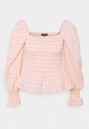Blouse manches longues en vichy pêche et blanc avec corsage smocké, encolure carrée, bas en volant et poignets élastiques.