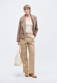 Pruun villaseguga topeltlapiga jakk, kreemjas top, beežid laiad püksid, beež käekott, pruunid pahkluu saapad, minimalistlik disain.