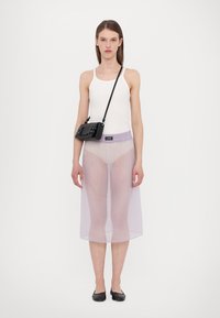 Průhledná světle fialová síťovaná sukně, bílý top bez rukávů a černá crossbody taška s texturovaným kovovým detailem, doplněné černými plochými botami.