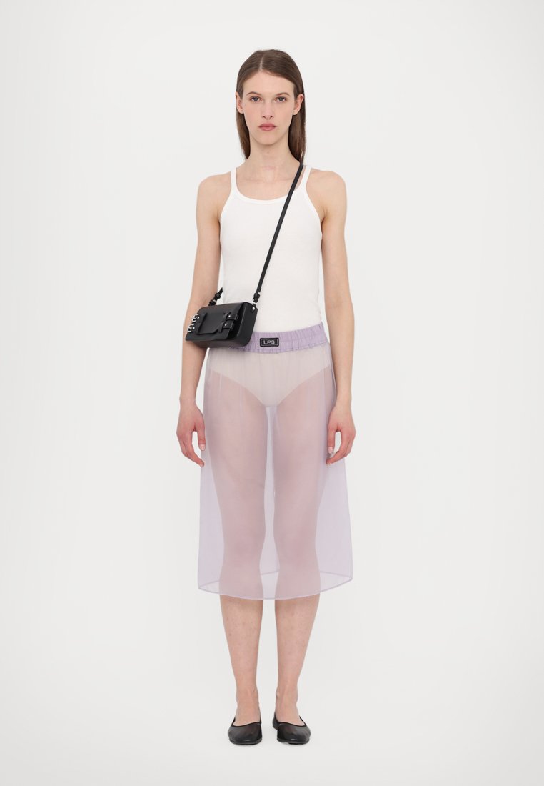 Jupe en maille transparentes de couleur violet clair, débardeur blanc et sac en bandoulière noir avec un détail en métal texturé, associé à des ballerines noires.