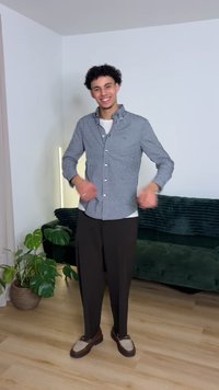 Checkered button-up shirt in navy and white, paired with loose brown trousers and slip-on shoes. Background features a green couch and plants.