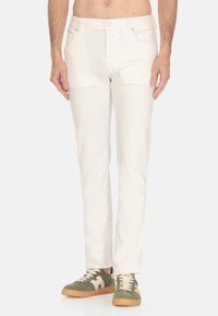 Pantaloni di cotone bianchi con design a gamba dritta, dotati di tasche frontali e chiusura con bottone, abbinati a sneakers verdi e beige.