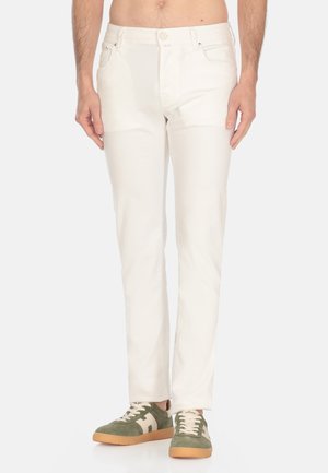 Pantaloni di cotone bianchi con design a gamba dritta, dotati di tasche frontali e chiusura con bottone, abbinati a sneakers verdi e beige.