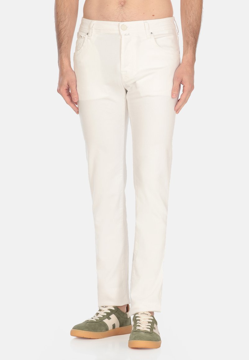 Pantaloni di cotone bianchi con design a gamba dritta, dotati di tasche frontali e chiusura con bottone, abbinati a sneakers verdi e beige.
