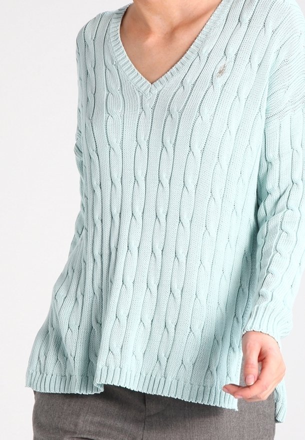 Ljusblå stickad tröja med V-ringning, med ett strukturerat kabelmönster och ribbad fåll. Lätt lös passform och långa ärmar.