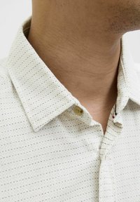 Chemise à boutons claire en tissu texturé, ornée d'un petit motif à pois répété dans des couleurs sombres et avec un design de col classique.
