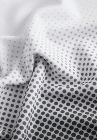 Textiltyg med en vit bas och en gradient av grå cirkulära prickar i varierande storlekar som skapar ett strukturerat mönster. Mjukt och slätt avslut.