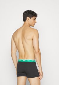 Boxer neri con elastico verde in vita e logo Nike. Tessuto morbido, design aderente, lunghezza a metà coscia.