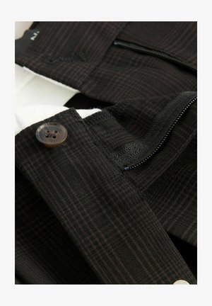 Black and brown plaid fabric with a visible button, zipper, and textured stitching details on a tailored garment.