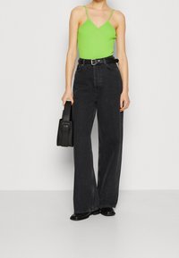 Zielony prążkowany body na cienkich ramiączkach, zestawiony z czarnymi, szerokimi spodniami z wysokim stanem. Trzyma małą czarną torebkę i nosi czarne botki.