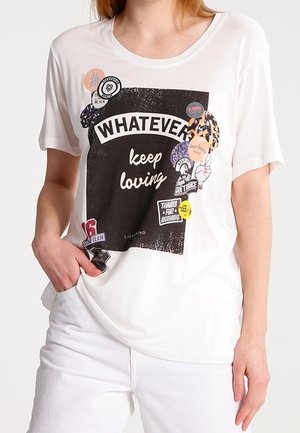Vrouw die een wit T-shirt draagt met een zwarte rechthoekige opdruk met de tekst "WHATEVER keep loving", versierd met verschillende kleurrijke sloganbadges.