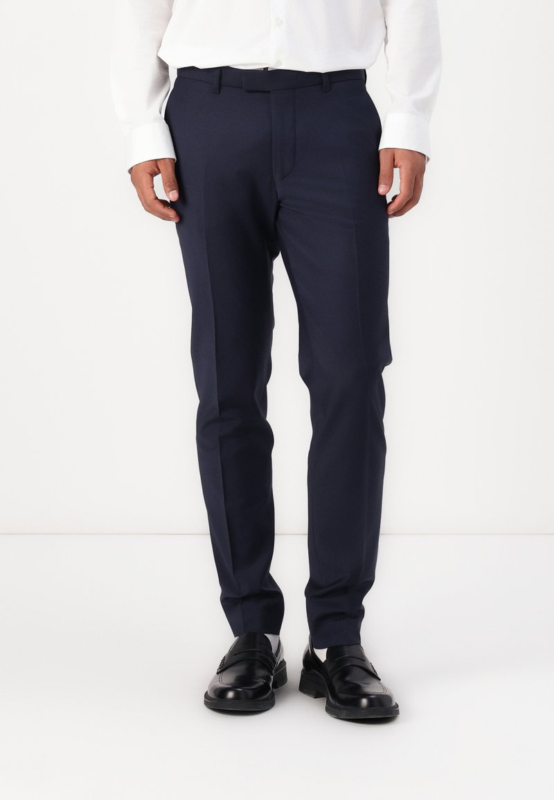 Pantalones navy a medida con un diseño elegante, que cuentan con un frente plano y dos bolsillos laterales, combinados con zapatos de cuero negros.