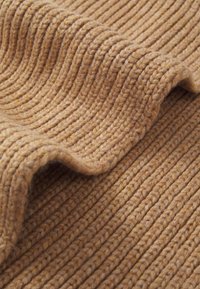 Tejido de punto acanalado marrón con textura visible y fibras suaves y peludas, mostrando un pliegue ondulado y detalles de costura ajustada.