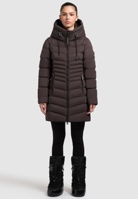 Dark brown padded coat with a fitted silhouette, vertical stitching, and a drawstring hood. Worn with black, ankle-high winter boots.