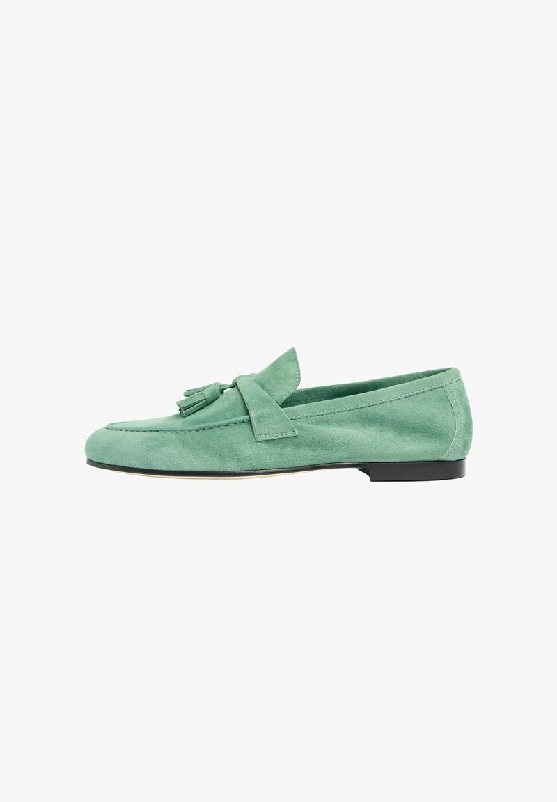 Mocassin en daim vert avec pampilles, petit talon noir et coutures décoratives sur fond blanc, vue de côté.