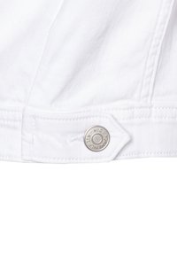 Tessuto denim bianco con un bottone argentato con inciso "Tommy Hilfiger NYC"; cuciture visibili lungo i bordi.
