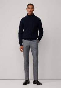 Pull en tricot torsadé bleu marine à col roulé associé à un pantalon tailleur gris clair et des chaussures en cuir noir. Design simple et texturé avec une silhouette ajustée.