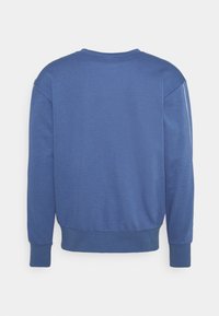 Sweat bleu à manches longues avec poignets et ourlet côtelés, montré de dos sur fond blanc.