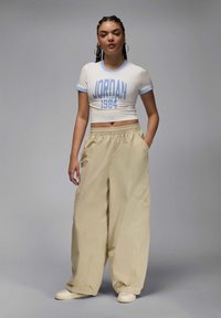 Skrócona biała koszulka z niebieskimi wykończeniami oraz grafiką "JORDAN 1984", połączona z luźnymi beżowymi spodniami cargo z bocznymi kieszeniami i elastycznym paskiem.