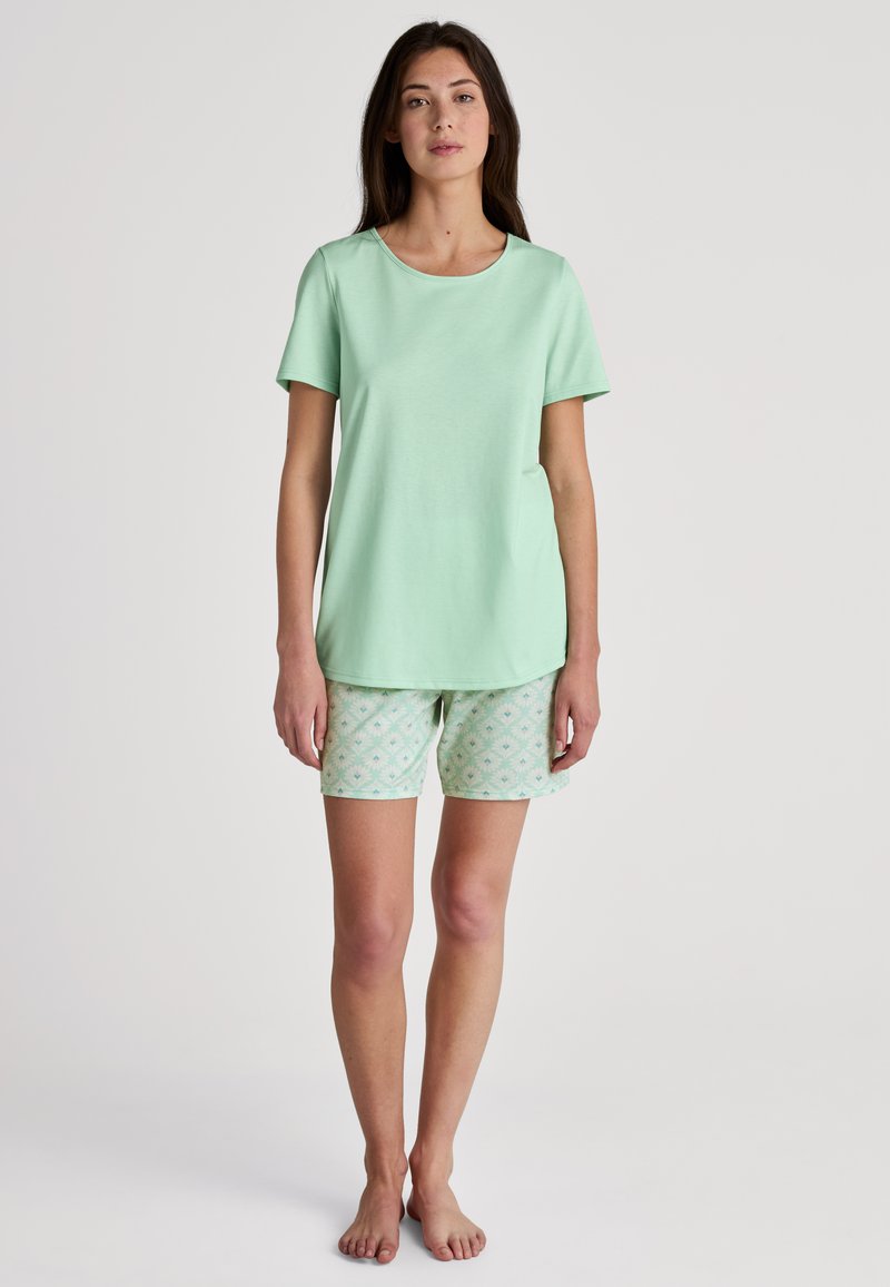 Mintgrünes T-Shirt mit kurzen Ärmeln, kombiniert mit gemusterten mintfarbenen Shorts, die florale Designs in hellen Farben aufweisen. Weicher, leichter Stoff.