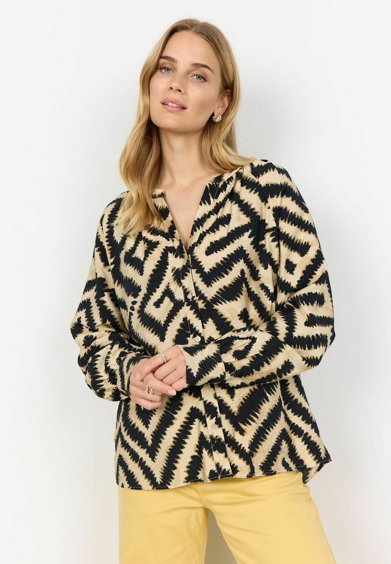 Chemise à manches longues boutonnée en beige avec un motif zigzag noir, dotée d'une coupe décontractée et d'un col, fabriquée à partir d'un tissu léger.