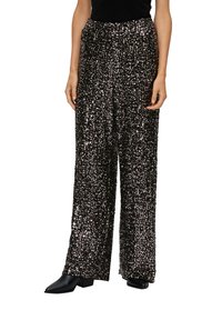 Schwarze Pailletten-Hose mit weitem Bein und lockerer Passform, die eine schimmernde Textur und ein hoch geschnittenes Design aufweist. Kombiniert mit schwarzen Ankle Boots.