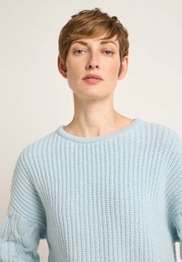 Hellblauer Strickpullover mit Rundhalsausschnitt, gerippter Textur und Zopfmusterakzenten an den Ärmeln. Weiches, gemütliches Material.