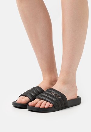 Schwarze Hausschuhe mit drei strukturierten Riemen, die das "ROXY"-Logo in erhabenem Detail tragen. Flache Sohle, minimalistisches Design.