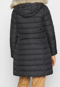 Abrigo negro acolchado con capucha, con borde de piel sintética, cintura ceñida y patrones de acolchado horizontal para aislamiento.