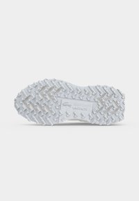 Semelle d'une chaussure blanche Lacoste avec un motif de bande de roulement en zigzag texturé et un logo Lacoste embossé au centre.