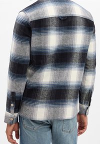 Plaid shirt in blue, black, and white with a button-down collar, long sleeves, and a soft texture. Features button cuffs and a back yoke.